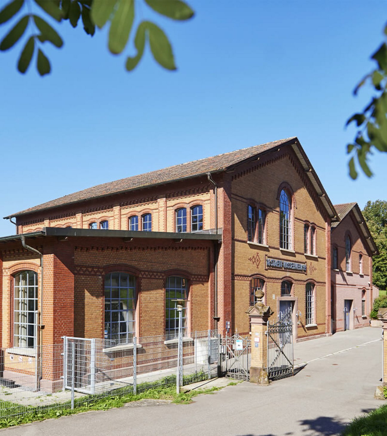 Das Wasserwerk Friedrichsberg Wasserwerks bei Sonnenschein, mit Einfahrtstor im Vordergrund.