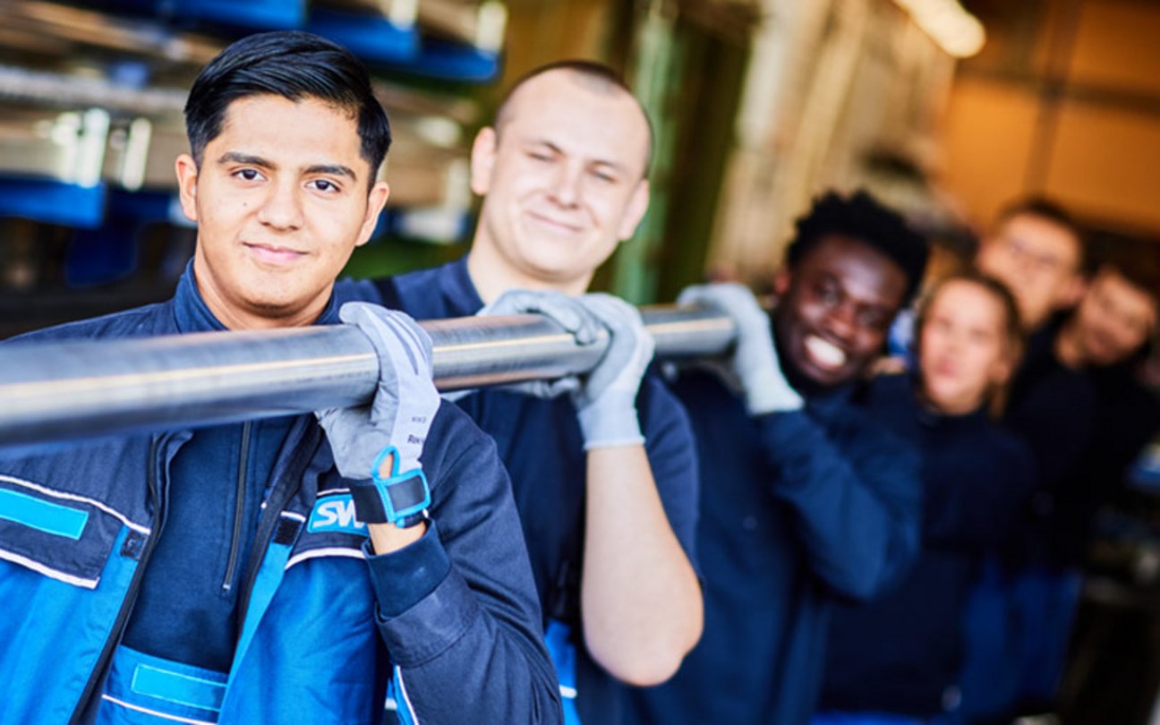 Das Bild zeigt mehrere Auszubildende, die ein Rohr tragen. 