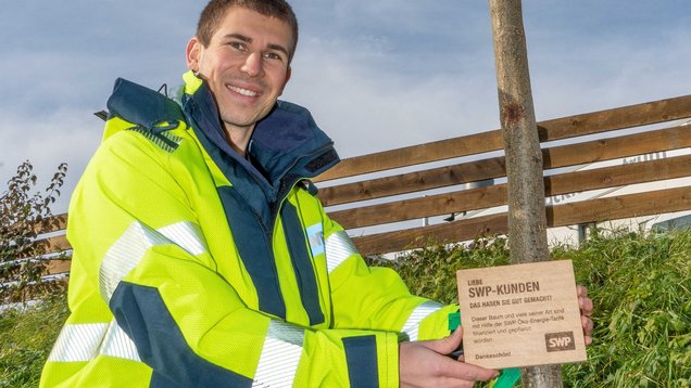 Das Bild zeigt unseren Kollegen nach dem Bäumepflanzen mit einem Schild in der Hand.