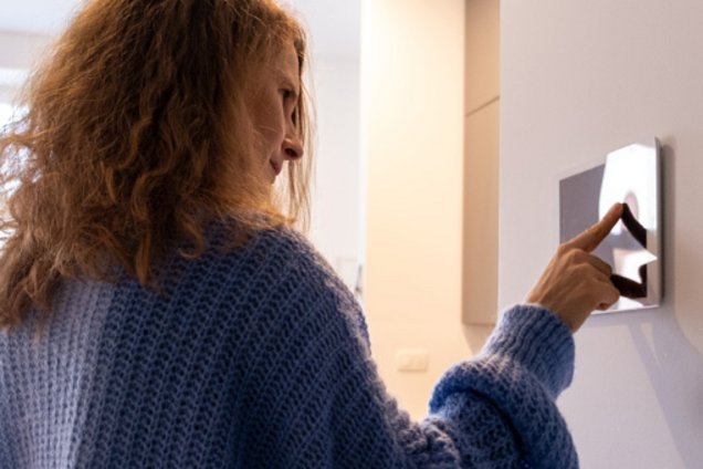 Frau tippt auf ein smartes Wandbedienfeld in einem modernen Raum.