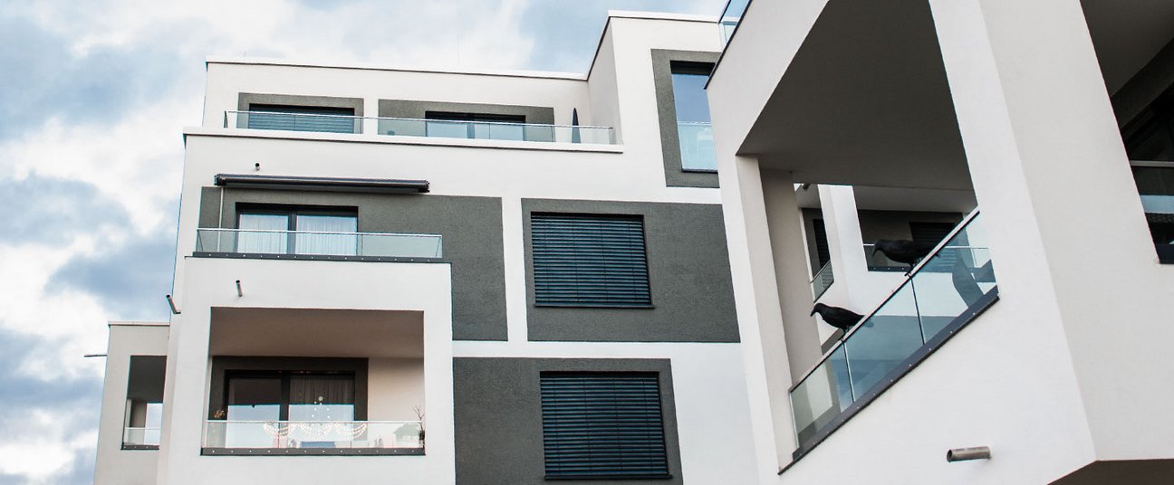 Das Einstiegsbild zeigt ein Mehrfamilienhaus von unten, man sieht vor allem die vielen schlichten Balkone.