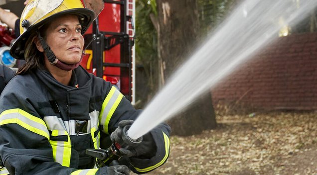 Feuerwehrfrau in Einsatzkleidung beim Löschen mit einem Feuerwehrschlauch