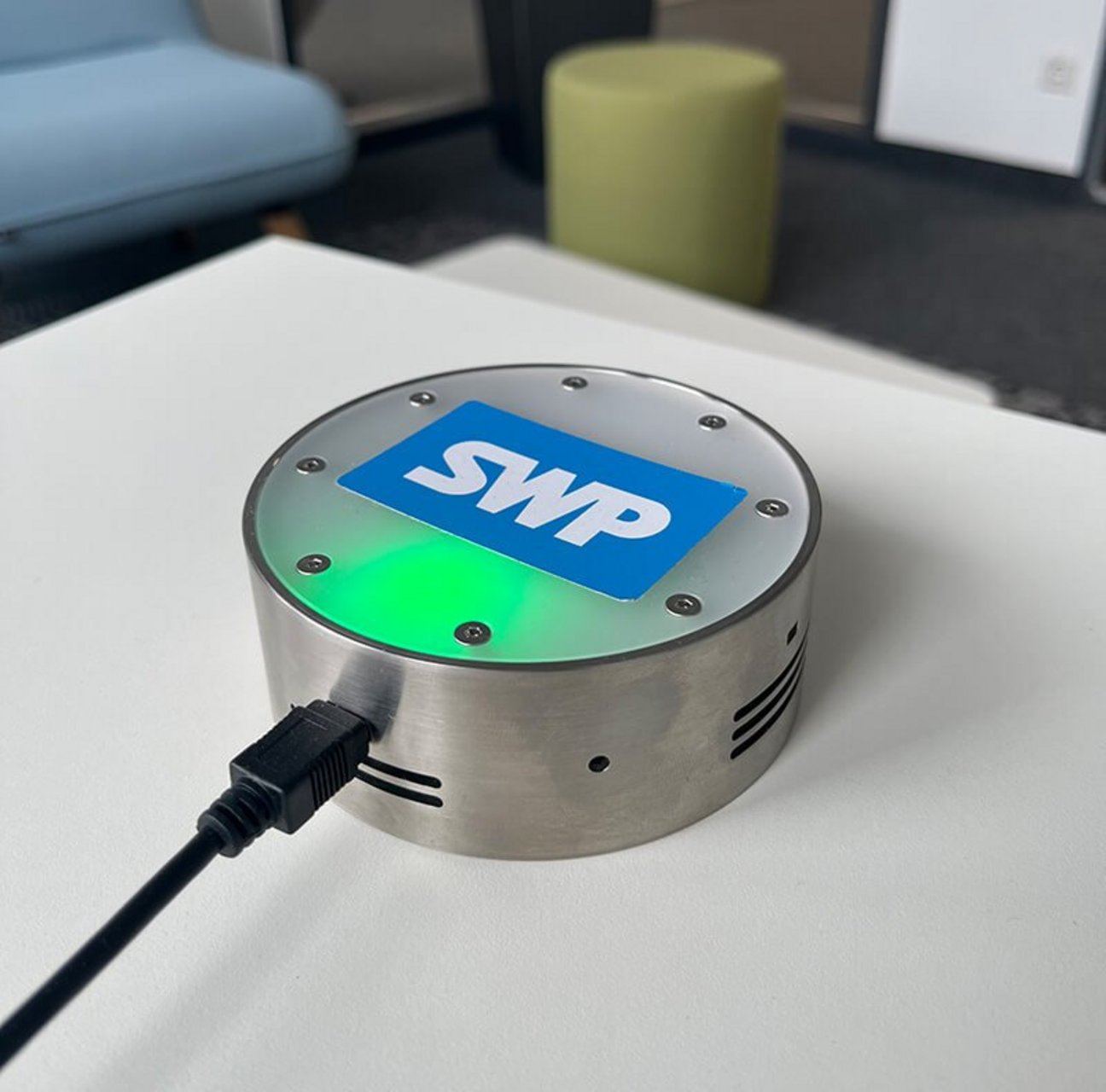Sensorgerät mit SWP-Logo misst Raumklima, platziert auf einem Tisch in moderner Büroumgebung.