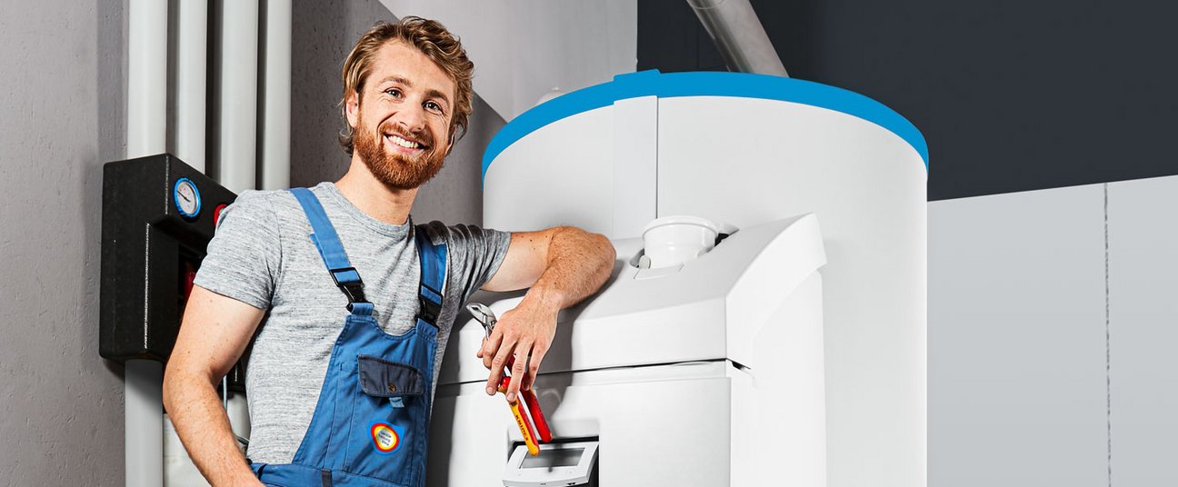 Das Bild zeigt einen Handwerker neben einer Fernwärmestation