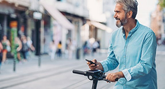 Das Bild zeigt einen jungen Mann der sich mit dem Handy durch die Smart City bewegt.