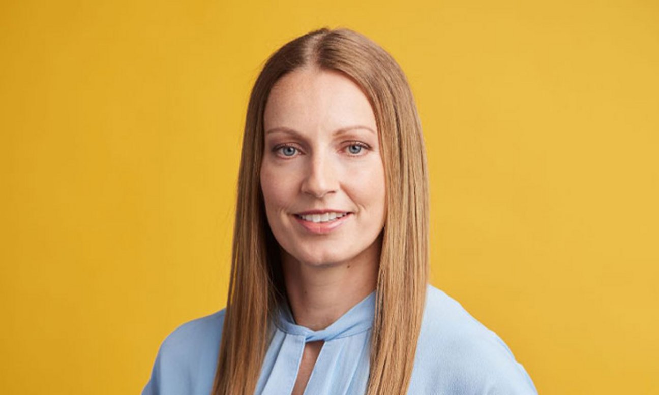 Bereichsleiterin für Vertrieb und Kundenservice Kerstin Eschler lächelt in die Kamera vor orangenem Hintergrund.