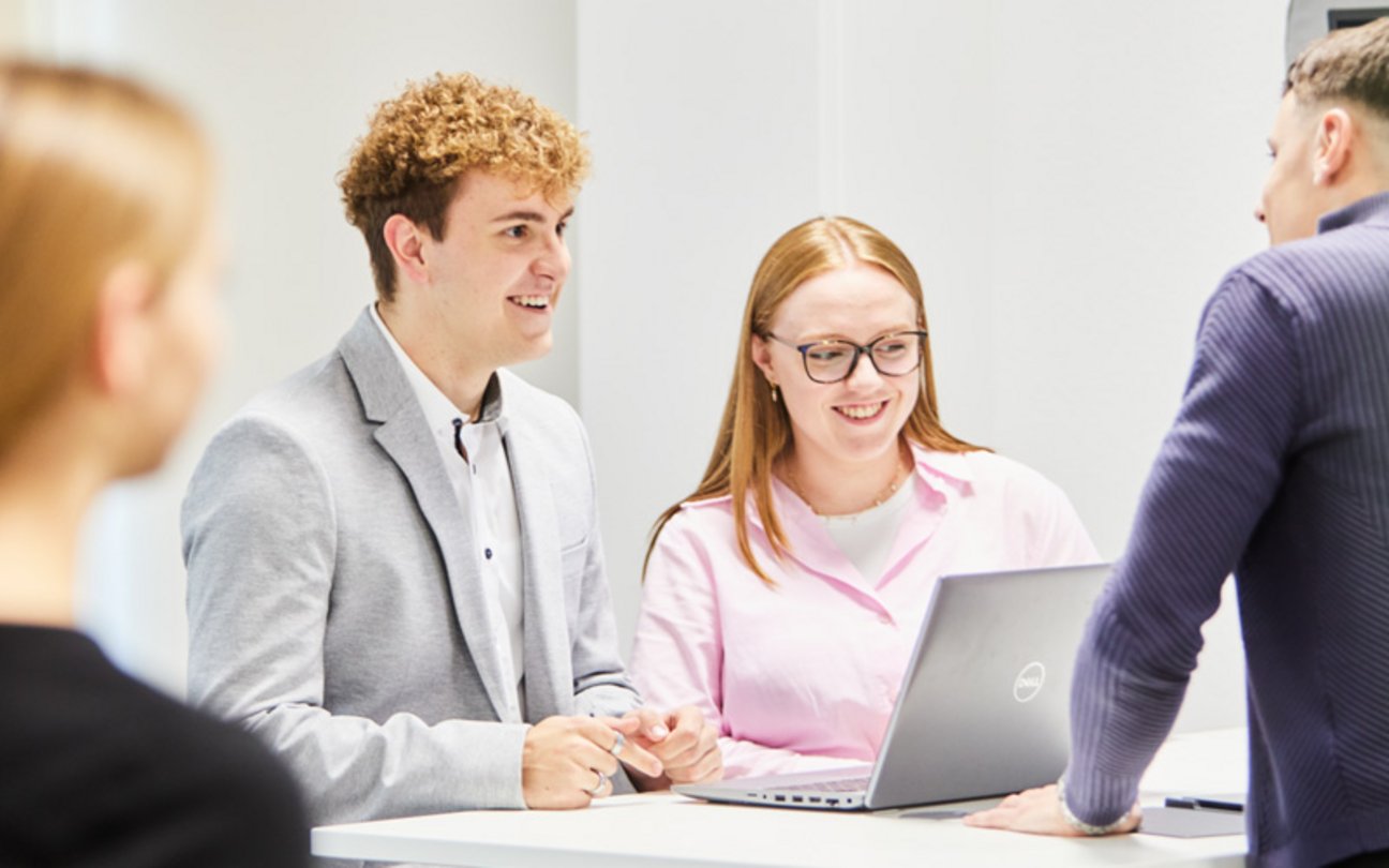 Das Bild zeigt zwei Auszubildende, die gemeinsam an einem Laptop arbeiten. 