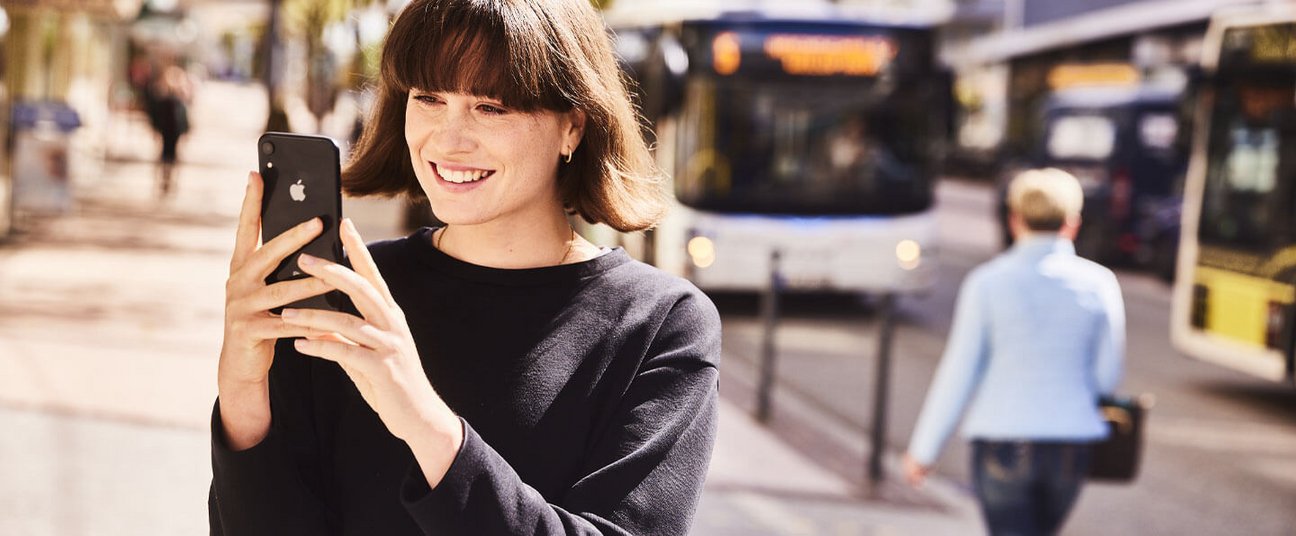 Das Einstiegsbild zeigt eine junge Frau die auf ihr Handy schaut und durch die Stadt läuft